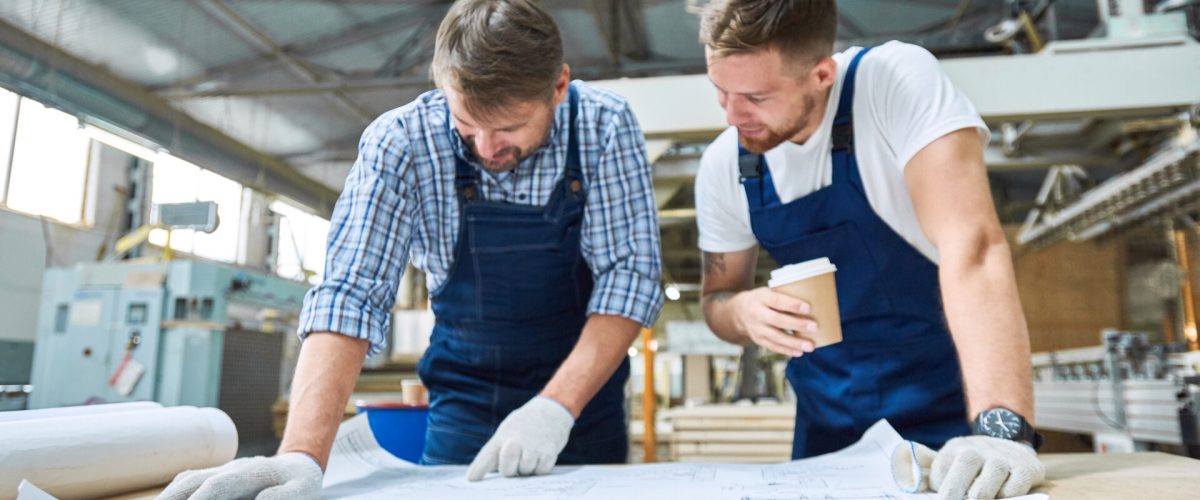 Frontalansicht Porträt zweier Arbeiter, die in der Werkstatt einer modernen Industriefabrik über Projektpläne diskutieren.